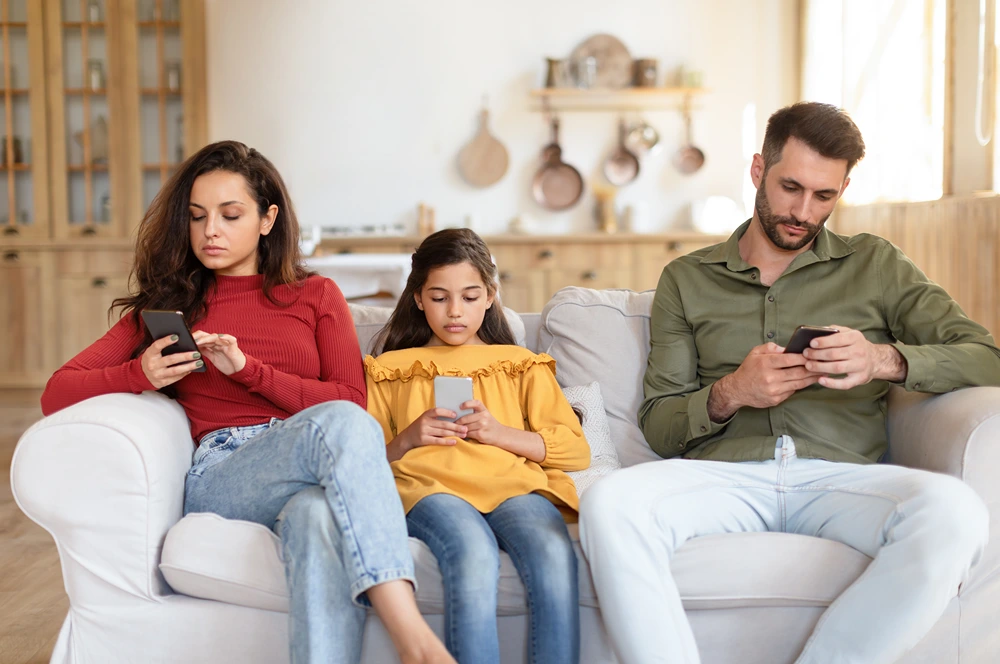 family using mobile phones on living room sofa